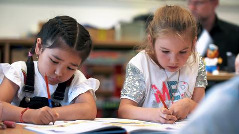 Zwei Grundschülerinnen sitzen an einem Tisch und schreiben konzentriert in ihre Hefte.