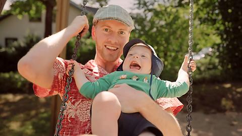 Vater mit Baby auf der Schaukel, beide lachen.